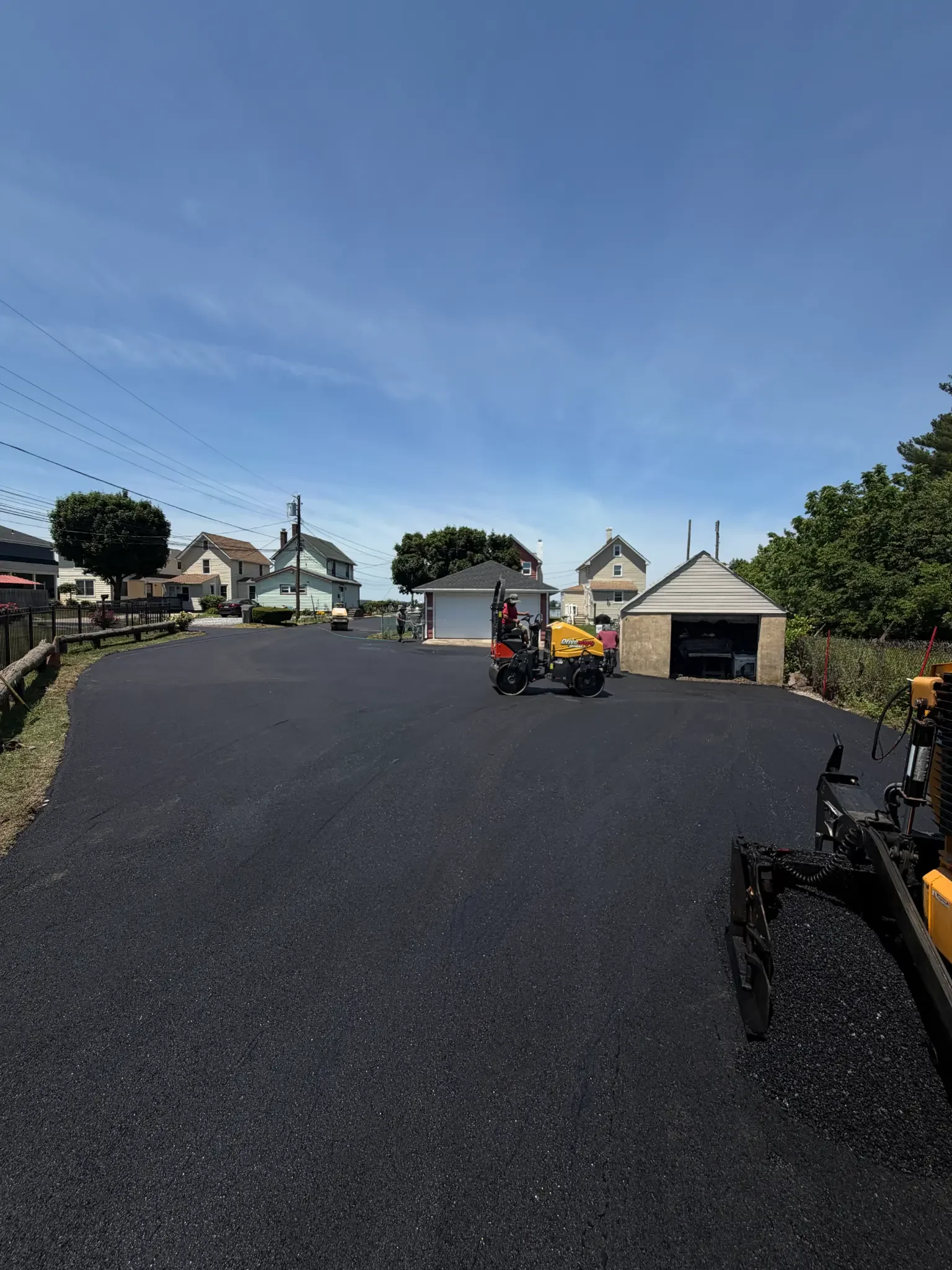 Newly paved asphalt driveway and parking area being compacted with a roller, with the paver in the foreground