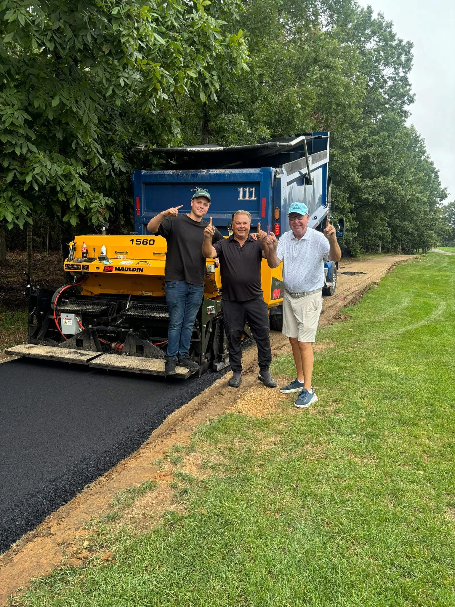 Three people standing beside an asphalt paver on a freshly paved private path