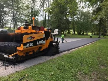 Asphalt paver laying a new driveway along a tree line
