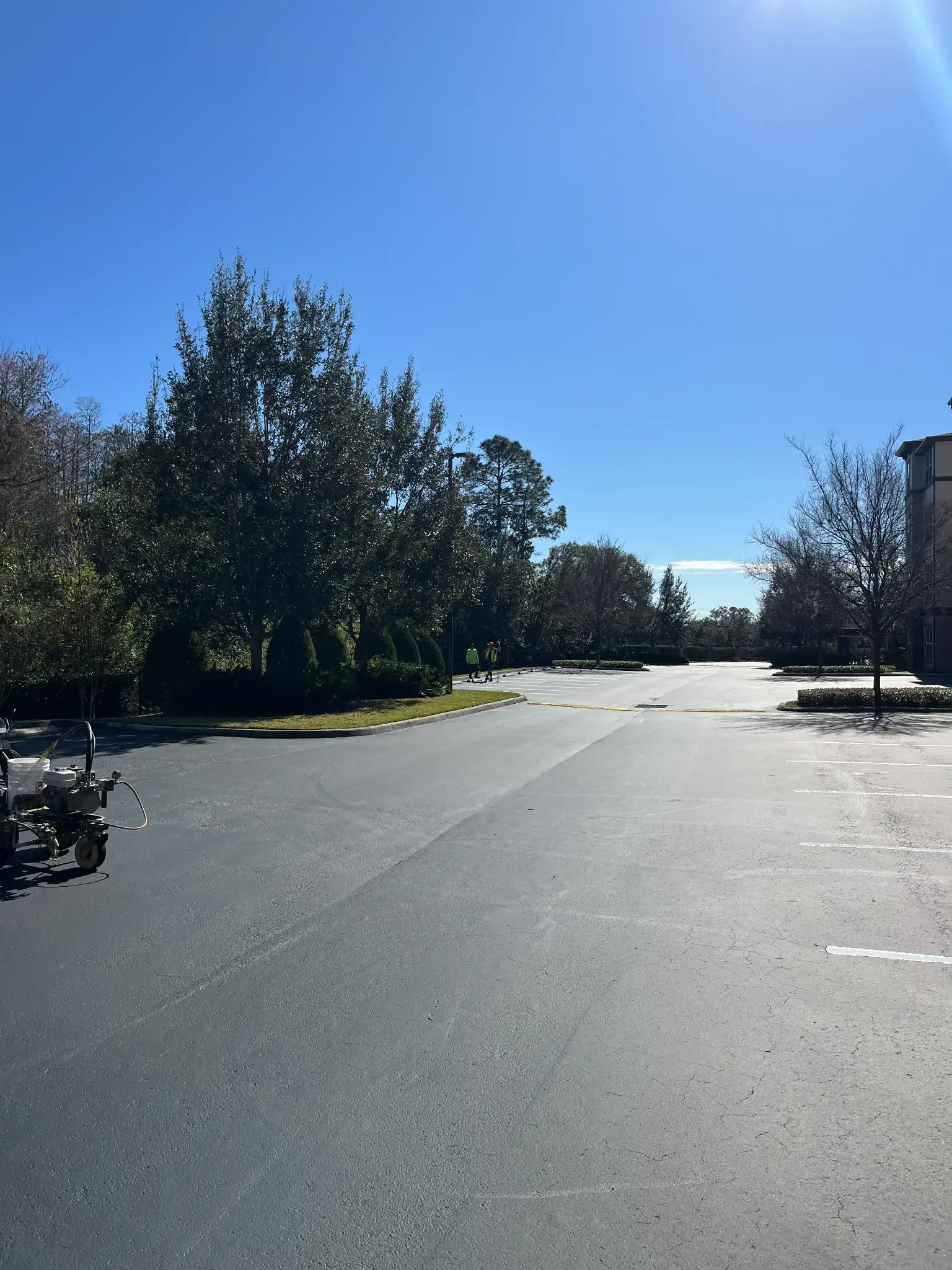 Freshly sealcoated commercial parking lot with a line-striping machine ready for new markings