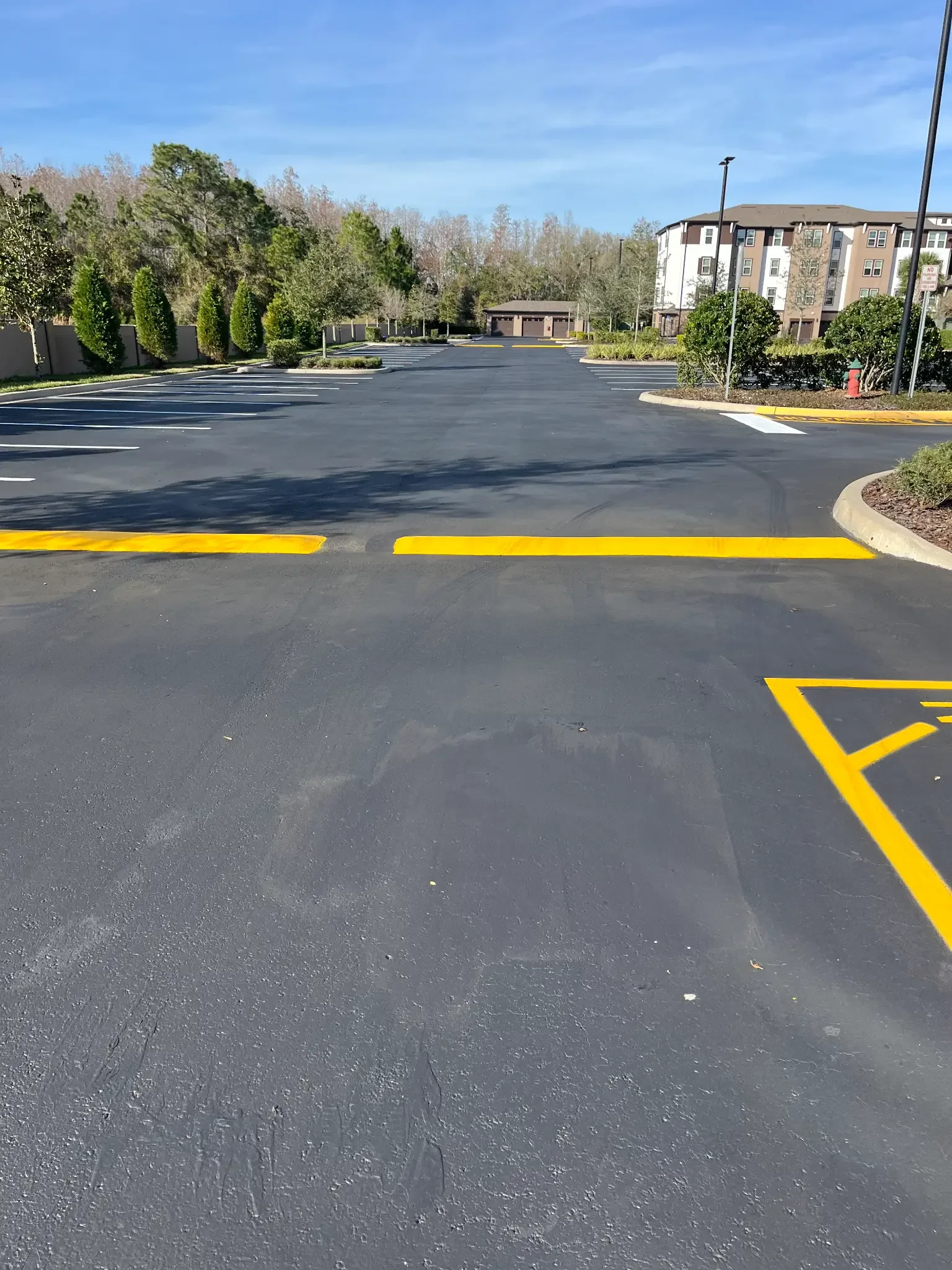 Sealcoated parking lot with new white stall striping and a freshly painted yellow speed bump